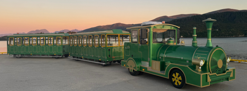 Green tourist train on a coastal path at sunset.