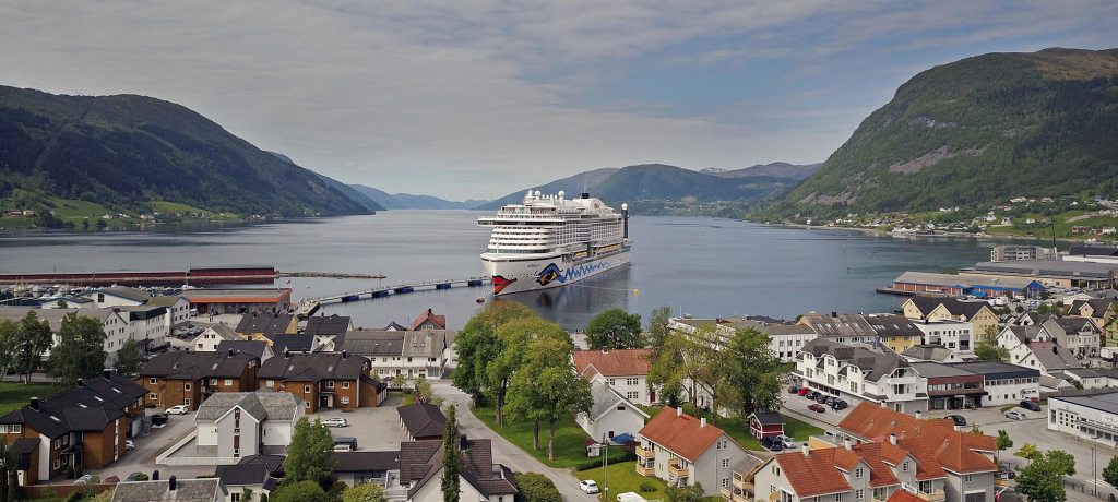 Cruise ship docked in a fjord town surrounded by mountains.
