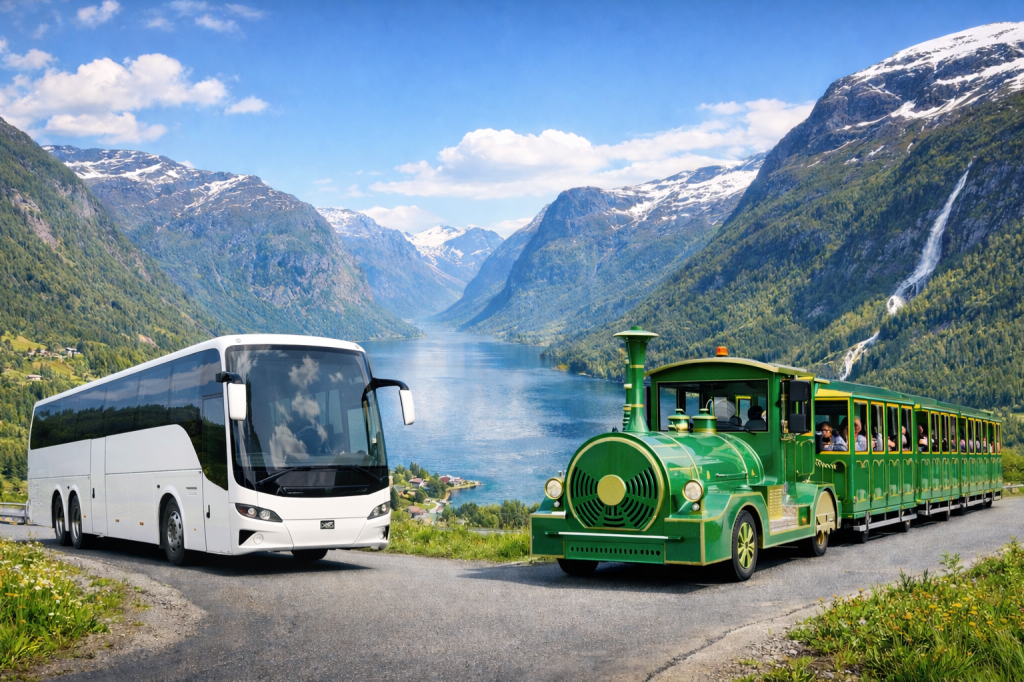 White bus and green tourist train with mountains and fjord backdrop.