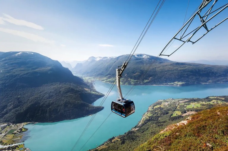 Cable car over turquoise lake with mountains and clear sky.