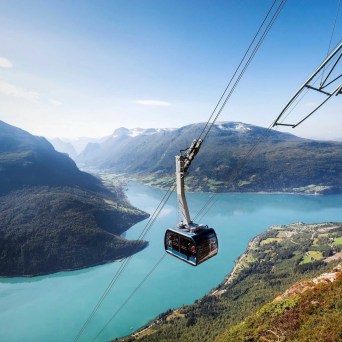 Cable car above blue fjord, surrounded by mountains and green landscape.