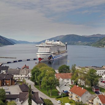 Cruise ship docked in a picturesque fjord town surrounded by mountains.