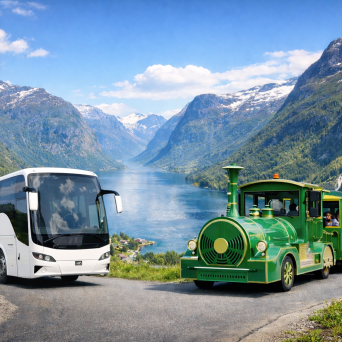 White bus and green tourist train on a road by a scenic fjord with mountains.